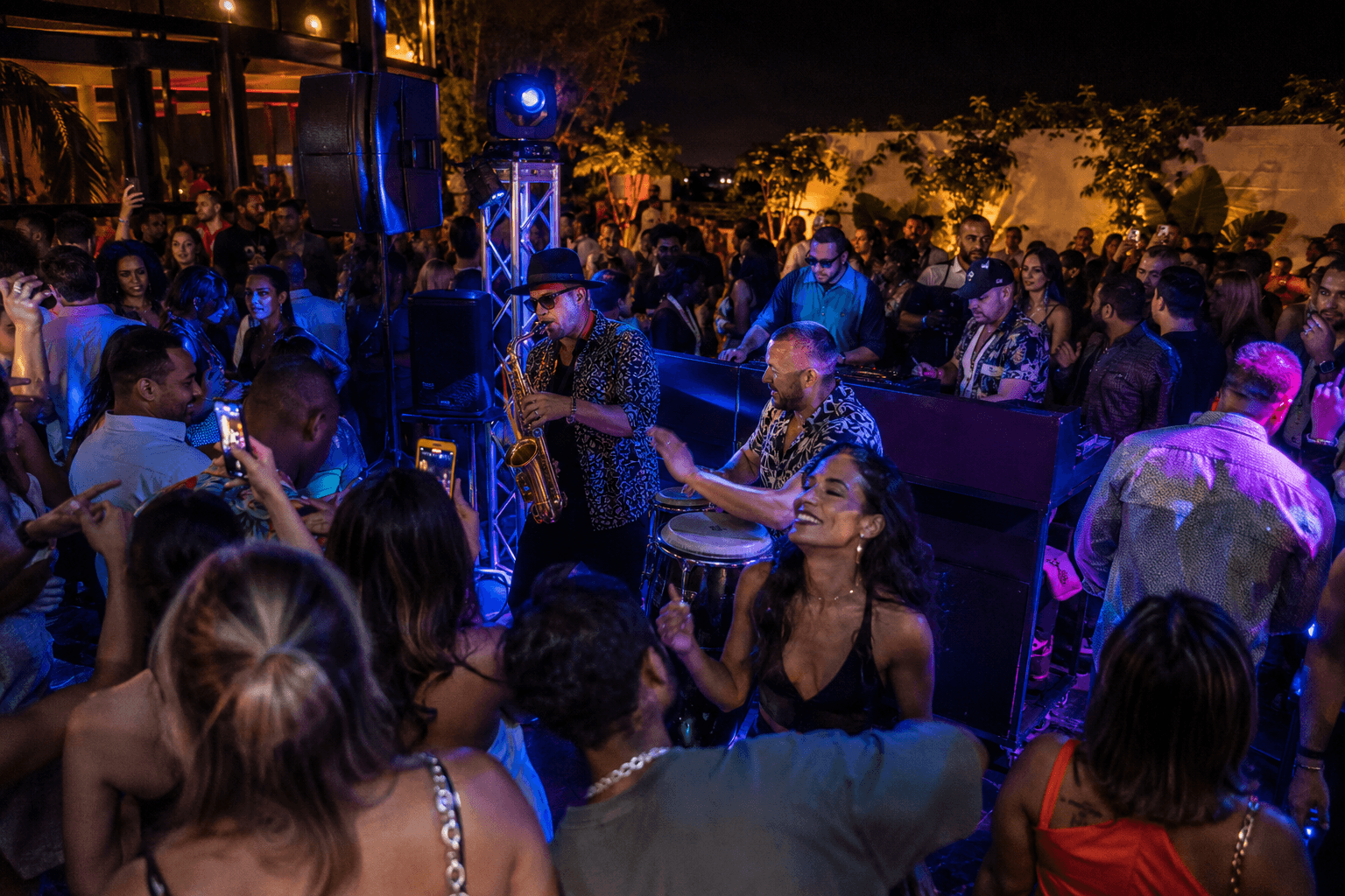 Conceptual scene — live saxophone player and percussion, guests dancing at night