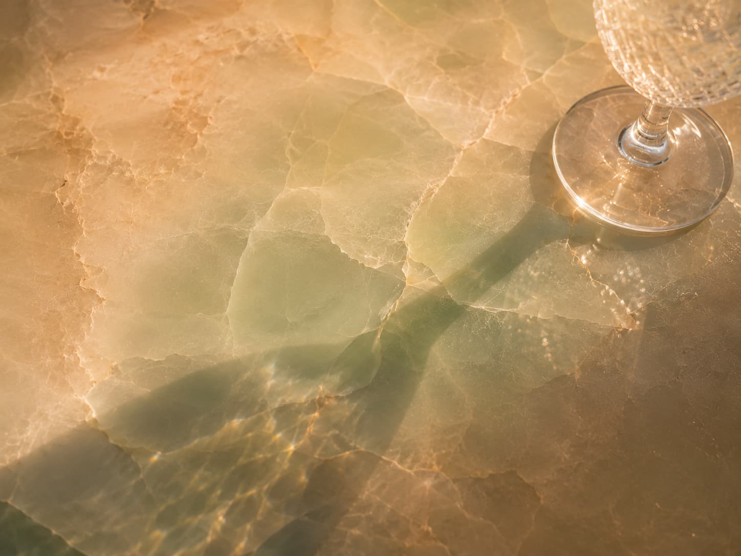 Close-up of the MAREA resin countertop — translucent, softly pearled with a trace of aqua, catching golden light under a glass